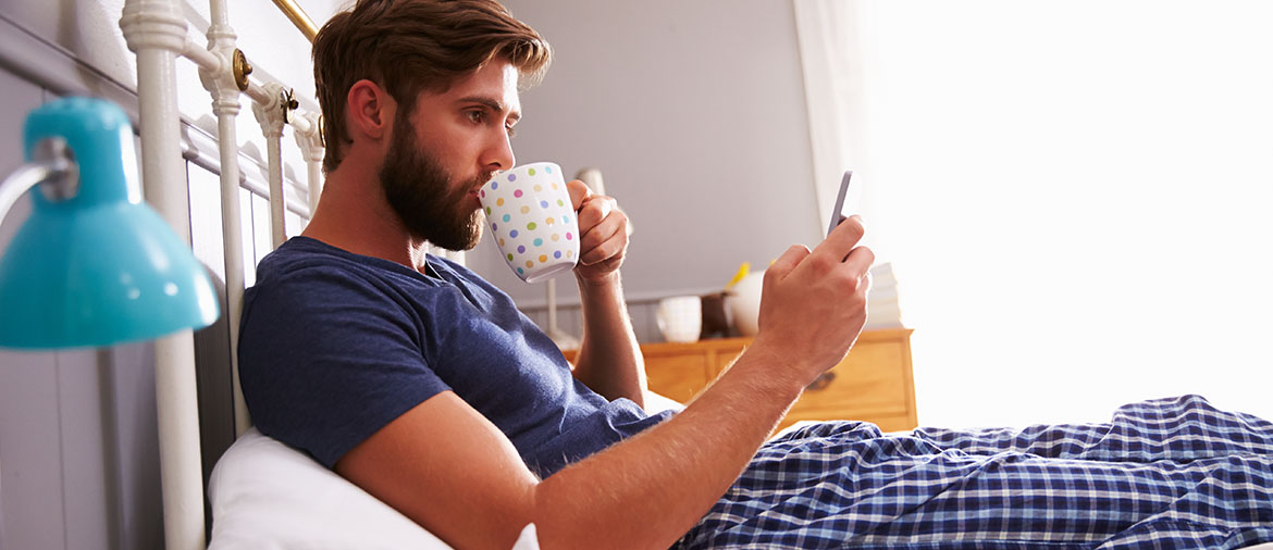 man in his pajamas sitting in bed drinking coffee